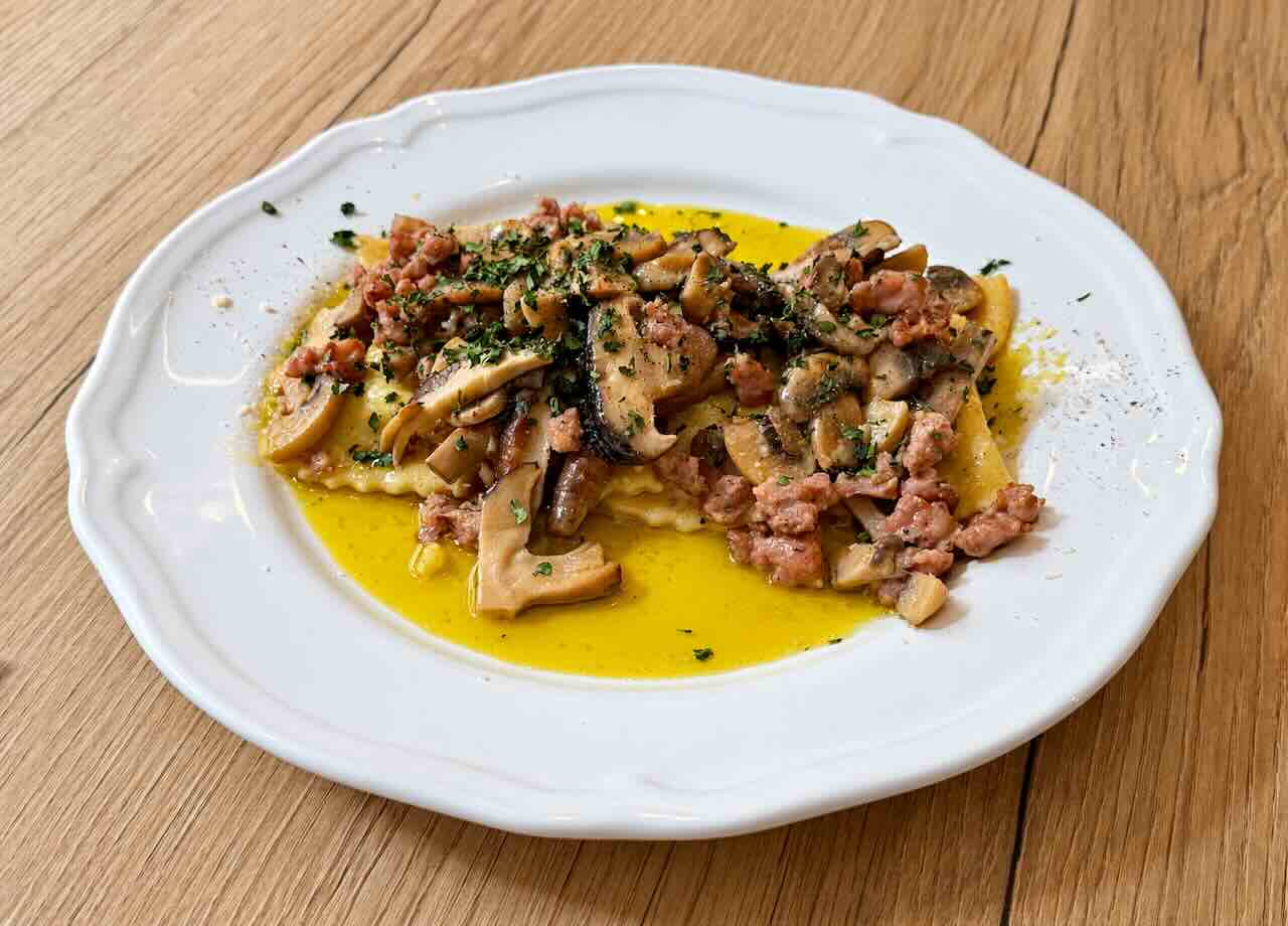 Ravioli del plin con setas y salchichas, servidos en un plato blanco en Nenét Bistrot, Santander.